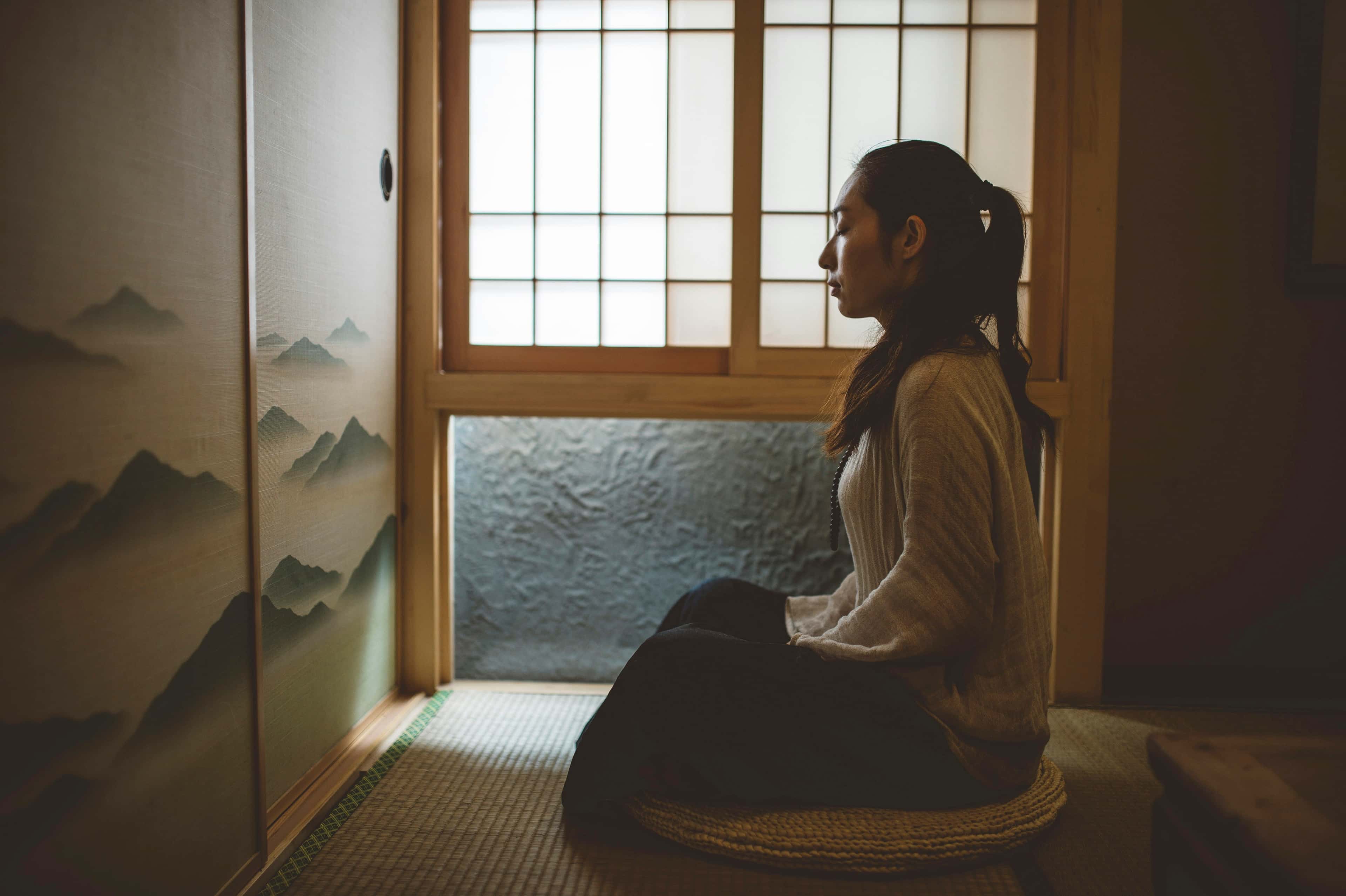 A calm room with paper screens and a woman seated on the floor by the window